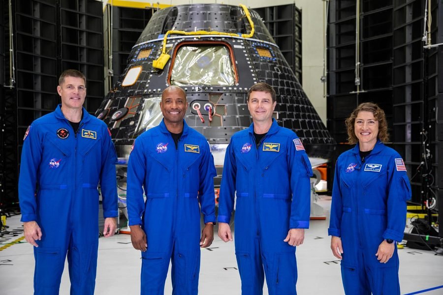 Artemis II crew standing in front of their Orion crew module at Kennedy Space Center